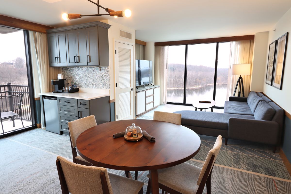 The Presidential Suite Living Room with a dining table, couch, tv, coffee station, mini fridge, and lake views.