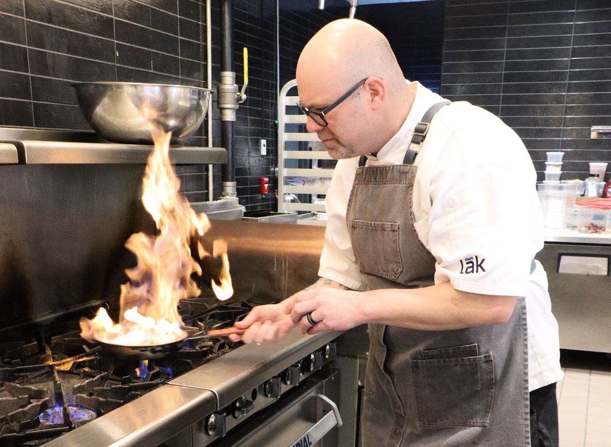 Chef Zach Dollak cooking over the lak stovetop with a flame. 