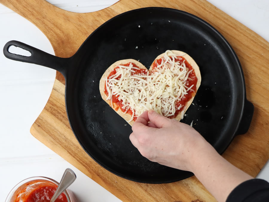 putting shredded mozzarella on a tortilla pizza on a skillet